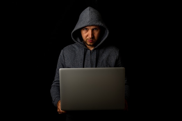 El hombre con capucha tiene una computadora portátil en sus manos en una oscuridad