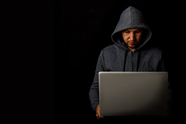 Foto el hombre con capucha tiene una computadora portátil en sus manos en una oscuridad