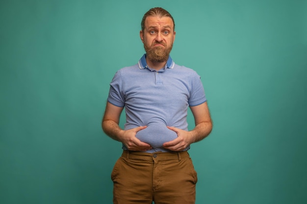 Un hombre con una cara triste siente su vientre gordo sobre fondo azul primer plano Espacio para texto