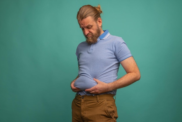 Un hombre con una cara triste siente su vientre gordo sobre fondo azul primer plano Espacio para texto