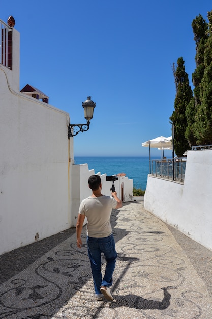 Foto hombre con cardán para smartphone caminando por las calles de una ciudad mediterránea