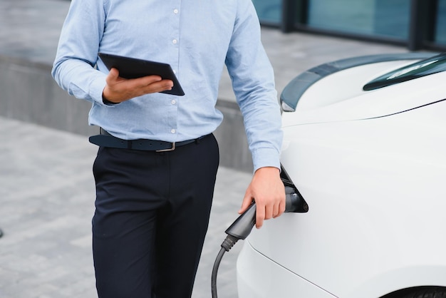 El hombre carga un coche eléctrico en la estación de carga