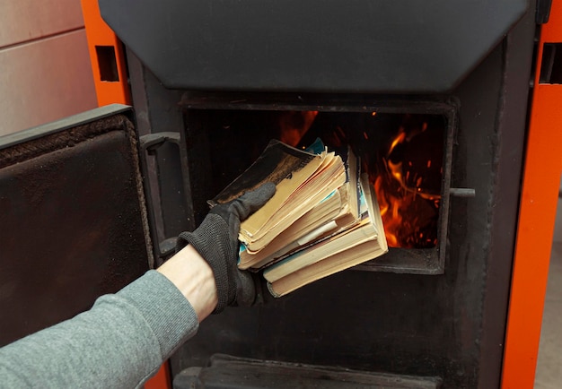 El hombre carga los libros antiguos en la caldera de combustible sólido en la sala de calderas Concepto de calefacción y combustible sólido