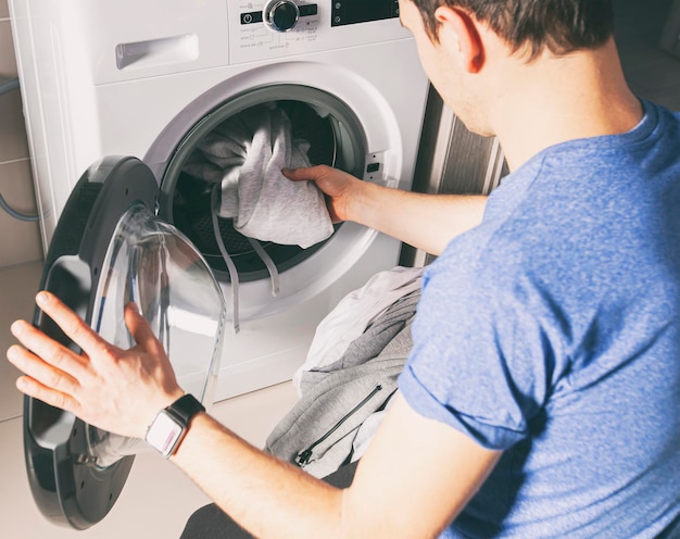 Hombre cargando la lavadora secadora con ropa