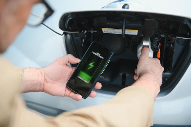 Hombre cargando vehículo eléctrico con cable mirando la aplicación en el teléfono móvil