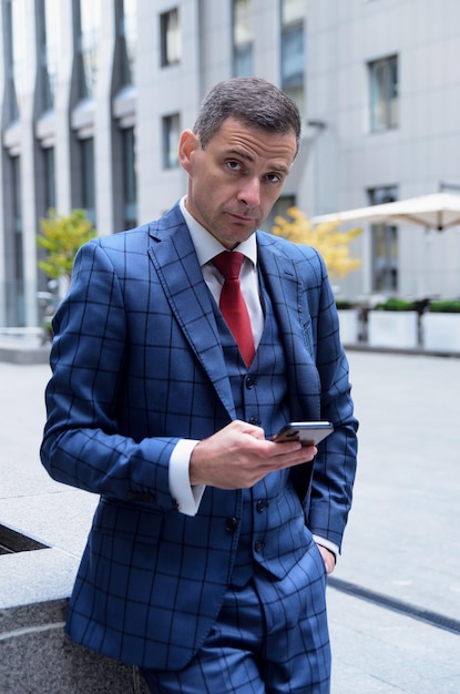 Hombre carismático en un traje a cuadros en el fondo de la oficina del centro de negocios Retrato de negocios de un elegante gerente de empleados de moda Envía mensajes por teléfono