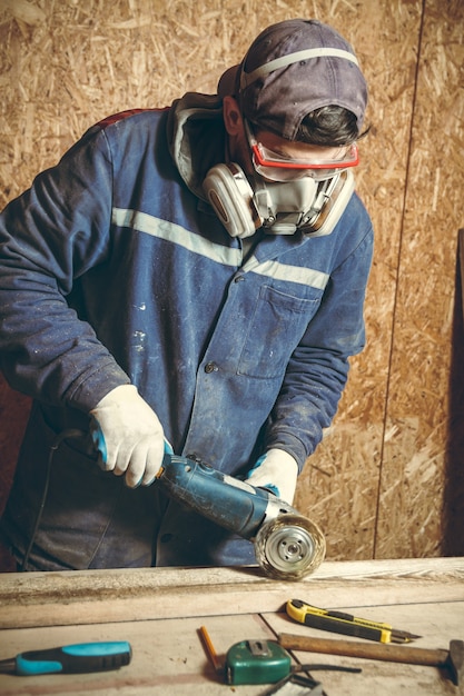 Hombre carpintero muele el trozo de madera con una rectificadora en el taller de su casa