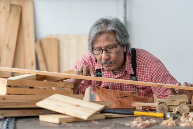 Hombre carpintero senior asiático mirando tablón de madera en el taller de carpintero