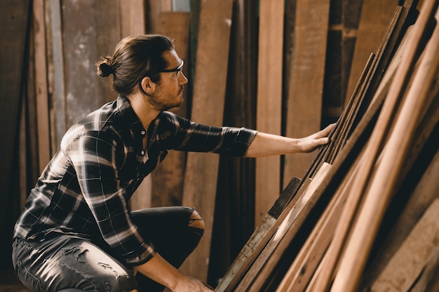 Hombre carpintero trabajando en el taller de muebles de madera, seleccionando tablero de madera.