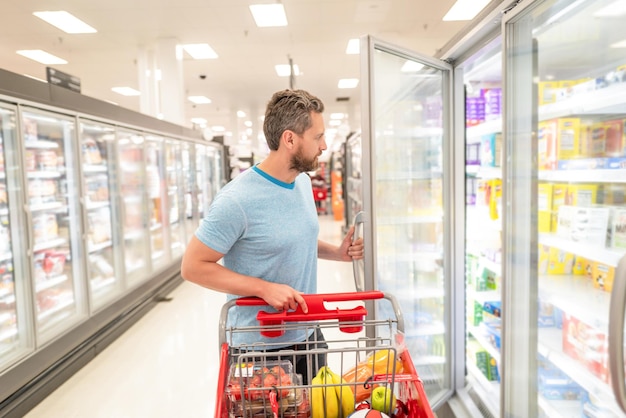 Hombre con carrito de compras comprando alimentos en el supermercado, consumo