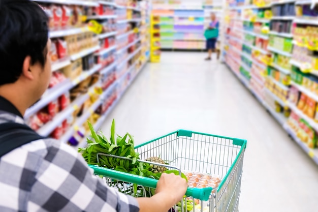 Foto hombre con carrito de compras comprando alimentos en un supermercado. detalle del primer del carro de compras.