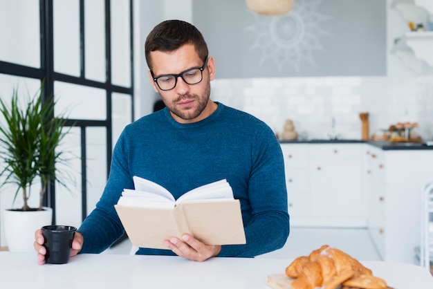 Hombre en casa con gafas leyendo libro