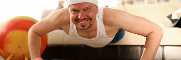 Hombre en casa haciendo flexiones en la alfombra y el sofá. Ejercicios para áreas problemáticas y entrenamiento de otros grupos musculares.