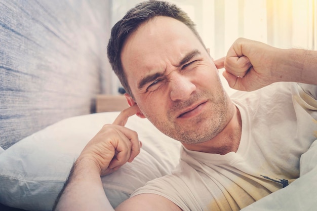 El hombre en casa intenta conciliar el sueño los vecinos ruidosos interfieren con el sueño un tipo cierra los oídos con las manos cansadas después del trabajo