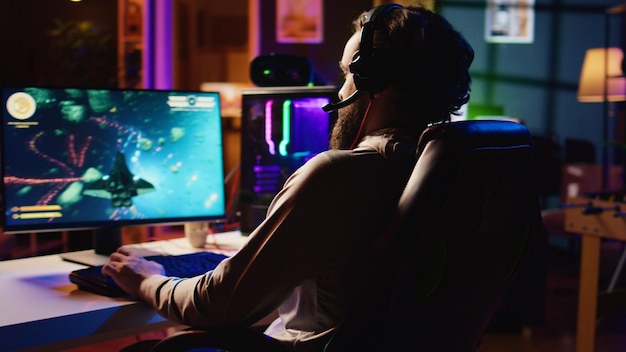 Hombre en casa jugando a un videojuego de un solo jugador con una nave espacial disparando rayos láser a asteroides