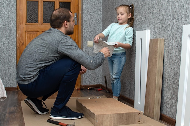 un hombre en casa recoge muebles con sus propias manos, su pequeña hija lo ayuda