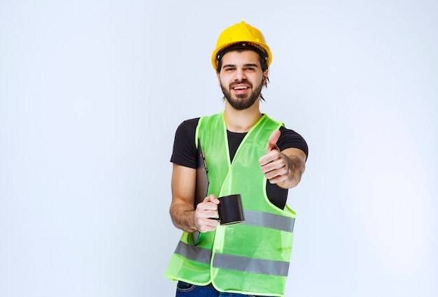 Hombre con casco amarillo con carpeta de proyecto y una taza de café.