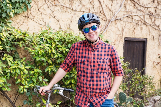 Hombre con casco y gafas permanecer en el jardín de la pared de la bicicleta