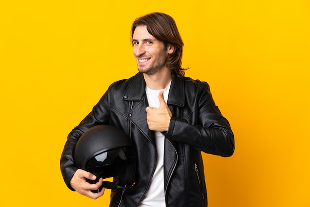 Hombre con un casco de moto aislado sobre fondo amarillo dando un pulgar hacia arriba gesto