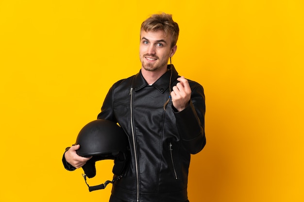 Hombre con un casco de moto aislado sobre fondo amarillo haciendo gesto de dinero