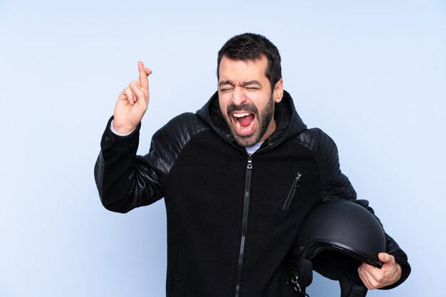 Hombre con casco de moto sobre pared aislada con dedos cruzando