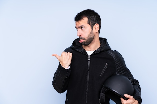 Hombre con casco de moto sobre pared aislada infeliz y apuntando hacia un lado