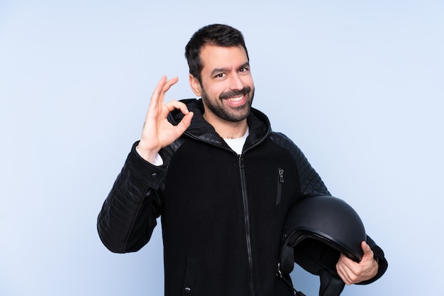 Hombre con un casco de moto sobre pared aislada mostrando signo bien con los dedos