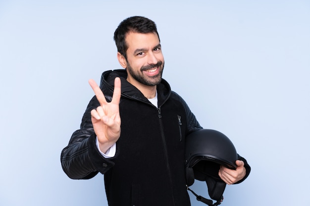 Hombre con casco de moto sobre pared aislada sonriendo y mostrando el signo de la victoria