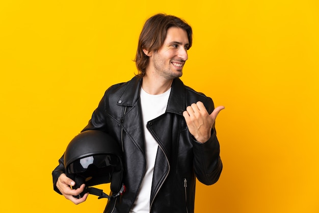 Hombre con un casco de motocicleta aislado sobre fondo amarillo apuntando hacia el lado para presentar un producto