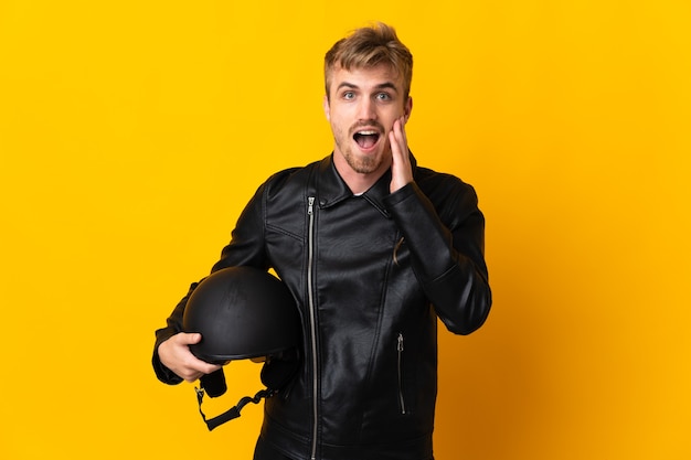 Hombre con un casco de motocicleta aislado sobre fondo amarillo con sorpresa y expresión facial conmocionada