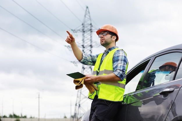 Un hombre con casco y uniforme, un electricista en el campo. El ingeniero electricista profesional inspecciona las líneas eléctricas durante el trabajo.