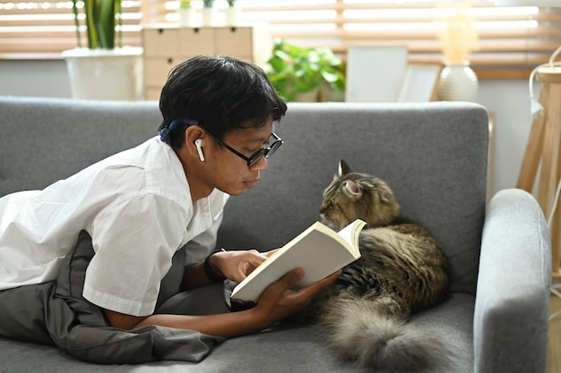 Hombre casual acostado en el sofá con su adorable gato y libro de lectura