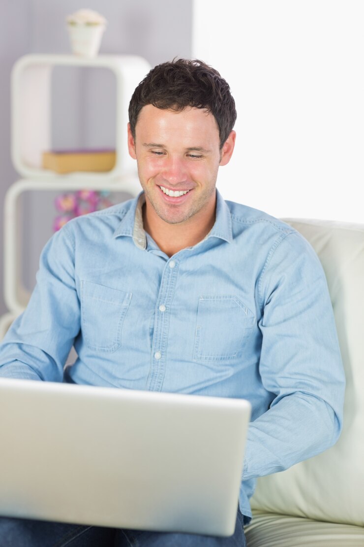 Foto hombre casual alegre que se sienta en el sofá usando la computadora portátil