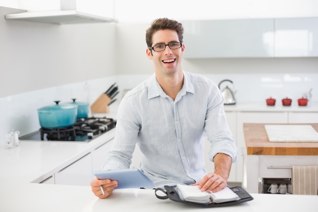 Hombre casual alegre con tableta digital y diario en la cocina