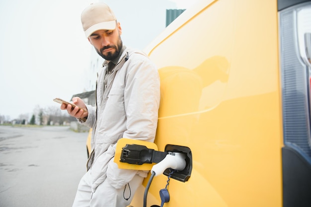 Hombre casual cerca del coche eléctrico esperando el final del proceso de carga de la batería