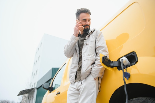 Hombre casual cerca del coche eléctrico esperando el final del proceso de carga de la batería