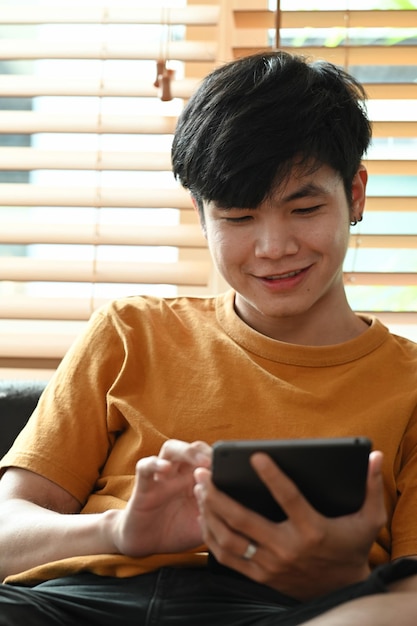 Un hombre casual feliz sentado en el sofá y navegando por una tableta digital