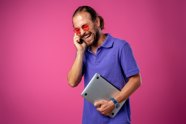 Hombre casual con gafas de pie con portátil contra rosa