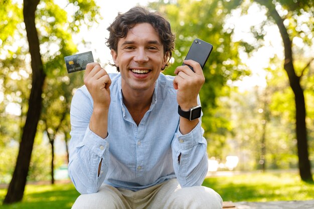 Hombre casual joven emocionado que sostiene el teléfono móvil