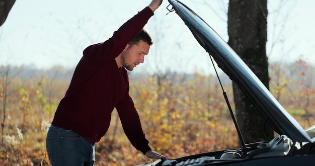 Foto hombre casual molesto joven que intenta arreglar su coche roto al aire libre. hombre esperando el servicio de remolque para ayudar a accidentes automovilísticos en la carretera. concepto de asistencia en carretera.