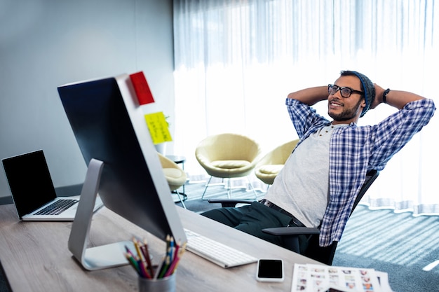 Hombre casual sonriente con las manos detrás de la mano descansando en el escritorio