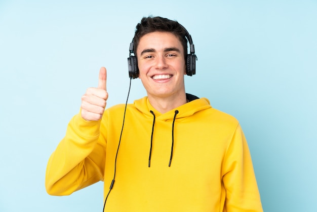 Hombre caucásico adolescente aislado sobre fondo púrpura escuchando música y con el pulgar arriba