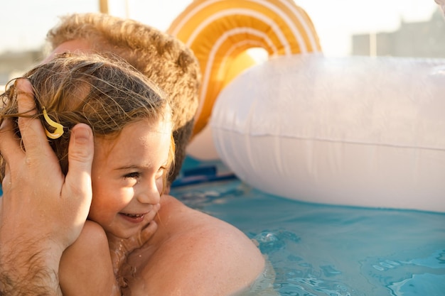 Hombre caucásico adulto besando a su hija de dos años nadando en la piscina jugando a su hijo