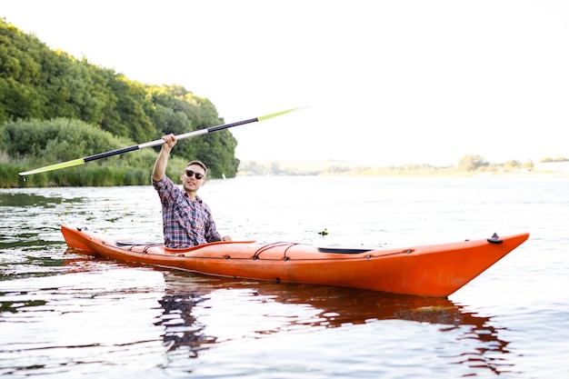 El hombre caucásico adulto está sentado en un kayak y saluda El concepto de las actividades acuáticas