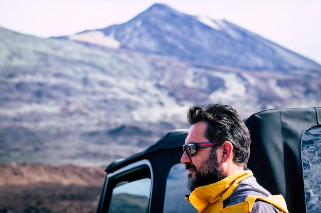 Hombre caucásico adulto guapo con barba y gafas de sol y montaña - concepto al aire libre de gente de aventura de viaje con coche todoterreno y equipo - estilo de vida activo