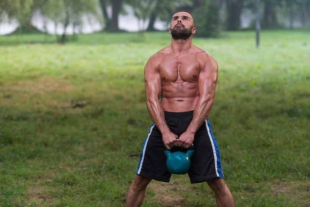 Hombre caucásico adulto musculoso haciendo un ejercicio al aire libre con pesas rusas