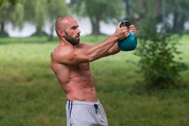 Hombre caucásico adulto musculoso haciendo un ejercicio al aire libre con pesas rusas