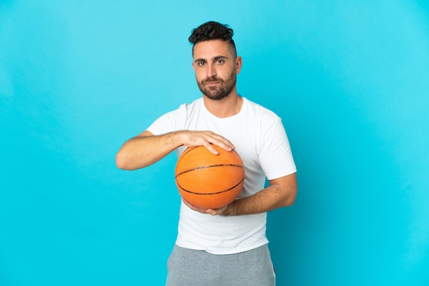 Hombre caucásico aislado sobre fondo azul jugando baloncesto