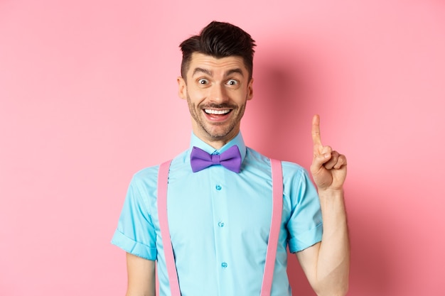 Hombre caucásico alegre lanzando una idea, levantando el dedo en gesto eureka y sonriendo, sugiriendo una solución, de pie sobre fondo rosa.