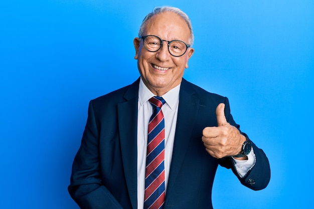 Hombre caucásico de alto rango con traje de negocios y corbata haciendo un gesto feliz con los pulgares hacia arriba con la expresión de aprobación de la mano mirando a la cámara mostrando el éxito